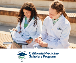 Two students in white lab coats reviewing notes together outdoors; California Medicine Scholars Program logo below