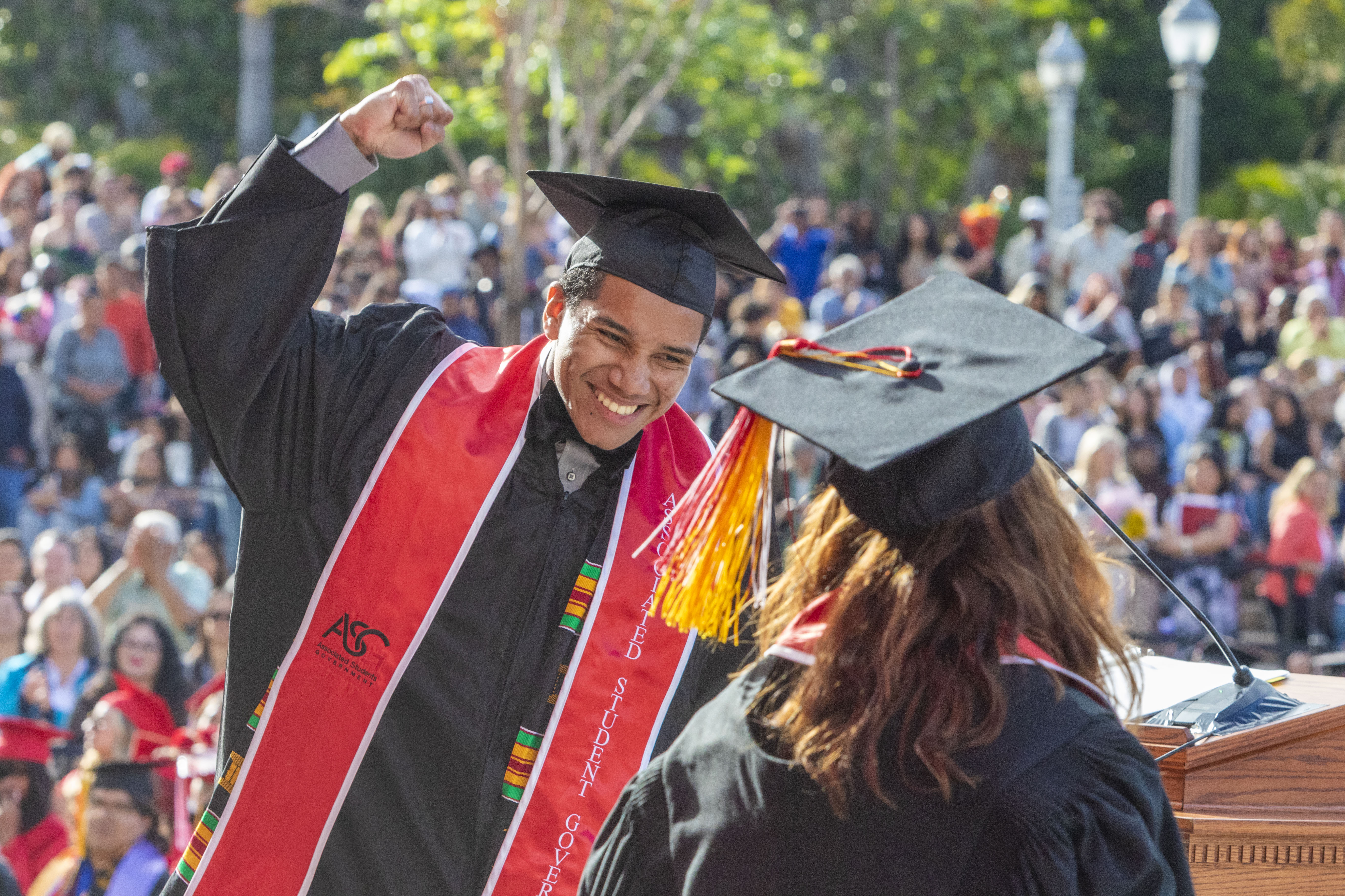 Male student smiling at graduation with fist in the air